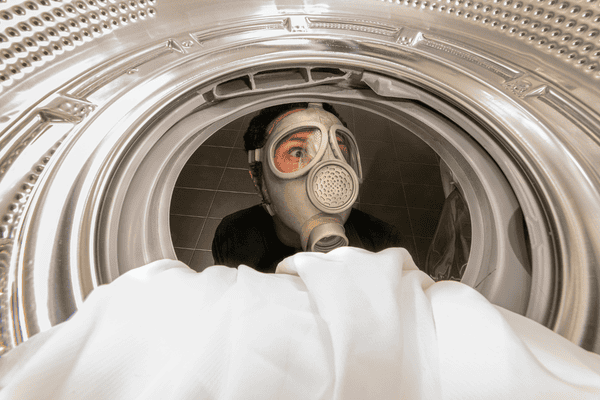 man with gas mask looking in washing machine smells moldy